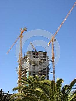 Cranes and under-construction apartment building against blue sky.