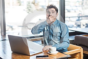 Crash! Side view portrait of emotional scared young businessman in blue jeans shirt are sitting in cafe and covering the mouth to