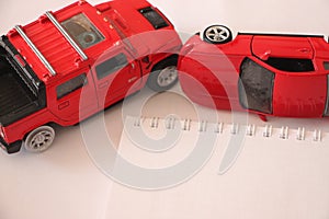 Crash between two toy cars isolated on white background and blank copybook for your notes. Road accident car insurance concept
