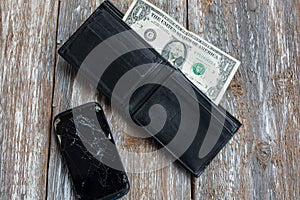 Crashed black smartphone is lying in an empty black leather wallet. One dollar in the purse. No money to buy a new phone. Poverty