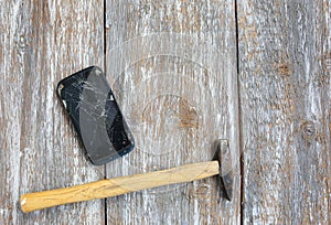 Crashed black smartphone is lying on the old wooden background. Broken lcd touch screen with a hammer. Information technology