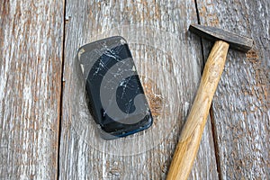 Crashed black smartphone is lying on the old wooden background. Broken lcd touch screen with a hammer. Information technology