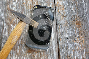 Crashed black smartphone is lying on the old wooden background. Broken lcd touch screen with a hammer. Information technology