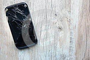 Crashed black smartphone is lying on the wooden background. Broken lcd touch screen. Information technology photo