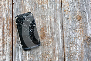 Crashed black smartphone is lying on the wooden background. Broken lcd touch screen. Information technology photo