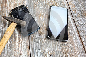 Crashed black smartphone is lying on the wooden background near the new phone. Broken lcd touch screen with a hammer. Information