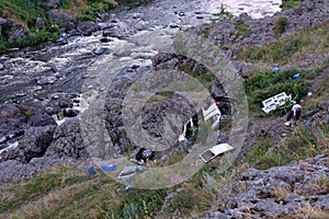 Crashed car near a mountain river with rapids, debris scattered all over the rocky shore on the Bank of trees