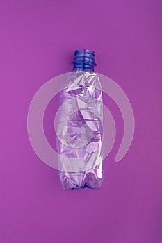 Crashed plastic bottle on blue purple background. Plastic utilisation concept. Ecological problem, global environment.