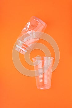Crashed plastic bottle and cup on orange background. Plastic utilisation concept. Ecological problem, global environment