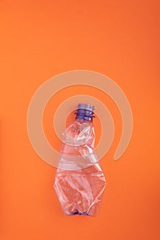 Crashed plastic bottle on orange background. Plastic utilisation concept. Ecological problem, global environment.