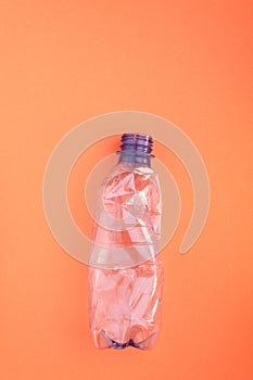 Crashed plastic bottle on orange background. Plastic utilisation concept. Ecological problem, global environment.