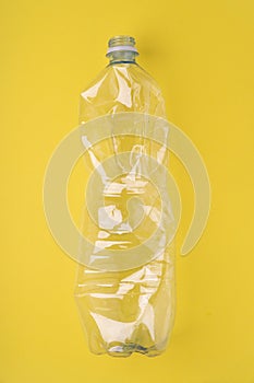 Crashed plastic bottle on yellow background. Plastic utilisation concept. Ecological problem, global environment.