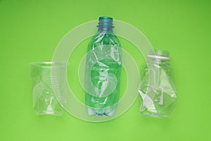 Crashed plastic bottles and a cup on bright green background. Plastic utilisation concept. Ecological problem, global