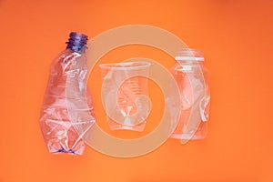 Crashed plastic bottles and a cup on orange background. Plastic utilisation concept. Ecological problem, global