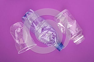 Crashed plastic bottles and a cup on purple background. Plastic utilisation concept. Ecological problem, global