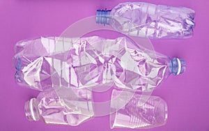 Crashed plastic bottles and a cup on purple background. Plastic utilisation concept. Ecological problem, global