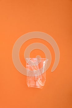 Crashed plastic cup on orange background. Plastic utilisation concept. Ecological problem, global environment.
