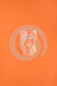 Crashed plastic cup on orange background. Plastic utilisation concept. Ecological problem, global environment.