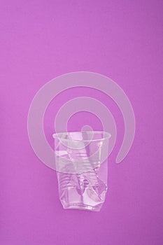 Crashed plastic cup on purple background. Plastic utilisation concept. Ecological problem, global environment.