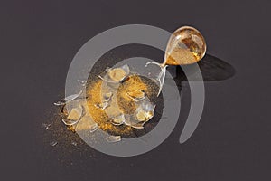 Crashed sandglass with golden sand on a black background.