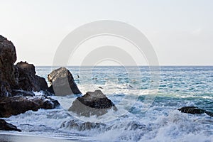 Crashing wave foaming past early morning lit boulders frothing on the beach