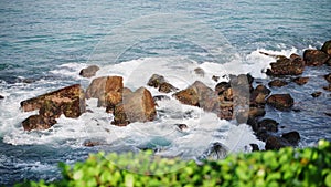 Crashing waves engulf rugged rocks along coastline. Seascape scene depicts natures power at seashore. Rocky shore washed