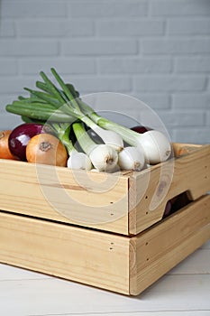 Crate with different kinds of onions on white wooden table