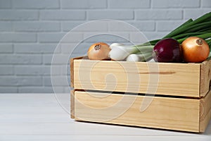 Crate with different kinds of onions on white wooden table, closeup. Space for text
