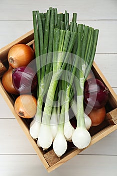 Crate with different kinds of onions on white wooden table, top view