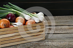 Crate with different kinds of onions on wooden table, closeup. Space for text
