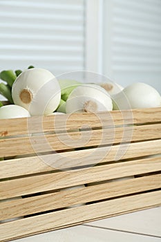 Crate with green spring onions on white wooden table, closeup
