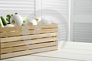 Crate with green spring onions on white wooden table, closeup. Space for text