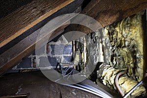 Crawl space under the eves of a house showing old fibreglass insulation, pipework, rafters, breezeblock construction and old board
