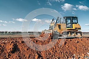Crawler bulldozer working on construction site or quarry. Mining machinery moving clay, smoothing gravel surface for new