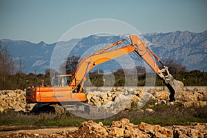 Crawler excavator clearing piles of rocks. Orange color machine