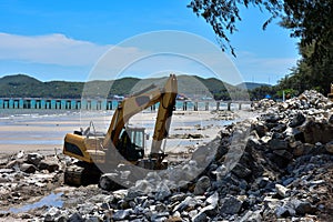 Crawler excavator are moving rocks to make breakwater on the beach