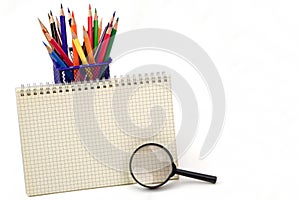 Crayon or colored pencils in box, graph book and magnifying glass is placed in front on white background.