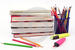 Crayon or colored pencils in box with side stack of books and school supplies on white background.