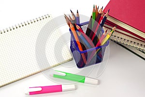 Crayon or colored pencils in box with side stack of books and school supplies on with background.