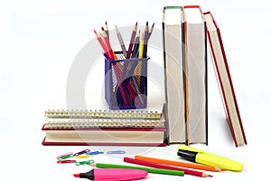 Crayon or colored pencils in box with side stack of books and school supplies.