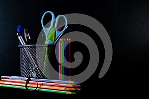 Crayons, Pencil colors, and a scissor with pen stand shot against a black background -Student Life concept