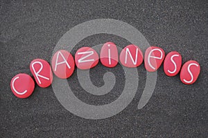 Craziness word composed with red colored and carved stone letters over black volcanic sand photo