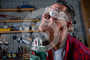 Crazy aggressive batty mad fun young man in plaid shirt, safety eye glasses on for protection, gloves with circular saw