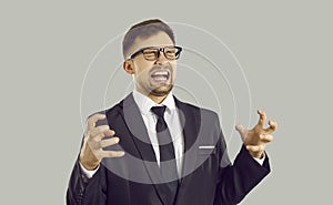 Crazy angry and frustrated young businessman shouting in anger isolated on gray background.