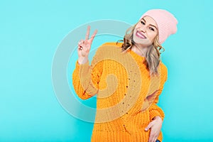 Crazy beautiful trendy girl in mustard coloured sweater and pink beanie hat making peace sign hand gesture. Cool young woman.