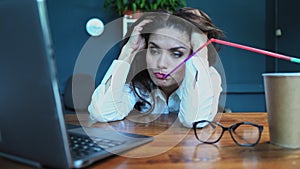 Crazy brown messy hair young freelance woman sit at the table in the office drinking water from a long straw trying to