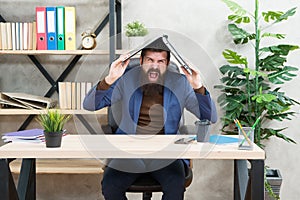 Crazy businessman in business suit shout loudly keeping notebook on head in modern office, desperation