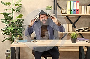 Crazy businessman in business suit shout loudly keeping notebook on head in modern office, desperation