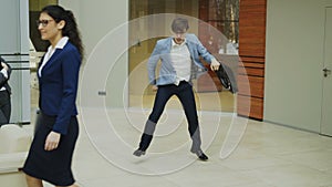 Crazy businessman dancing with briefcase in modern lobby while his colleagues walking and watching him surprised