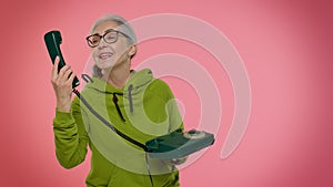 Crazy elderly granny old woman talking on wired vintage telephone of 80s, fooling making silly faces